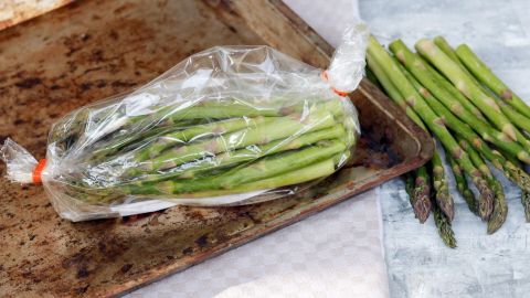 Grüner Spargel in einer Plastiktüte liegt auf einem Backblech, während frischer Spargel daneben ausgebreitet ist.