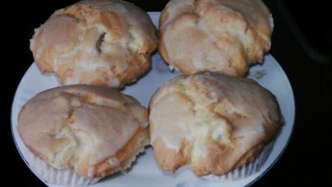 Vier Rhabarber-Muffins liegen auf einem Teller, umhüllt von hellem Teig mit glasiger Oberfläche, vor dunklem Hintergrund.