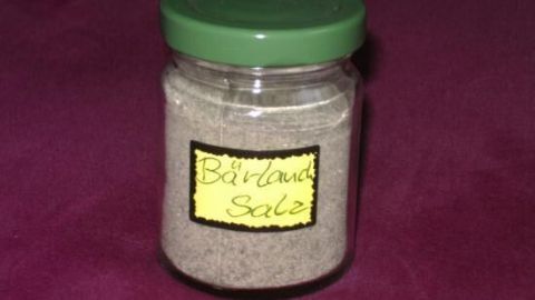 Ein Glas mit grünem Deckel enthält Bärlauchsalz, steht auf einem dunklen Tuch. Auf dem Glas steht handgeschrieben "Bärlauch Salz".