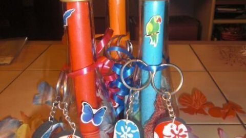 Die Flaschenpost ist eine kreative Einladung zur Hawaii- oder Sommerparty. In bunten Röhren versteckt, zieht sie alle Blicke auf sich und macht Lust auf einen unvergesslichen Tag voller Spaß und Sonne. Lass dich inspirieren! Bunte Flaschenpostrollen stehen in einer Gruppe, umgeben von sommerlichen Accessoires. Schlüsselanhänger in Flip-Flop-Form hängen daneben.