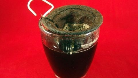 Ein Glas mit schwarzem Tee steht auf einem roten Hintergrund. Der Tee wird in einem speziellen Filter zubereitet.
