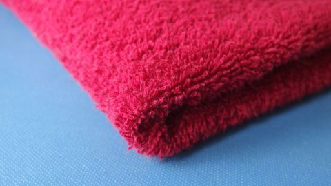 Ein rotes Frotteehandtuch liegt auf einer blauen Oberfläche und vermittelt ein Gefühl von Weichheit und Farbe.