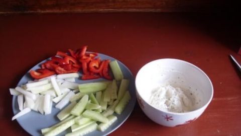 Auf einem Holzuntergrund liegen frische Gemüsesticks aus Paprika und Sellerie neben einer Schüssel mit cremigem Frischkäse-Dip.