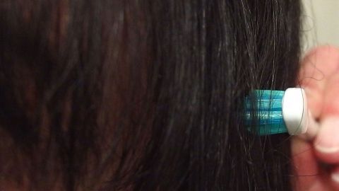 Ein Pinsel mit blauer Borsten kommt in Kontakt mit dunklem Haar, während eine Person eine Frisur ohne "Tentakel" kreiert.