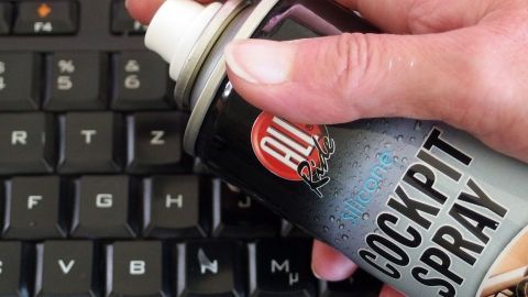 Eine Hand hält eine Dose Cockpit-Spray über einer Computer-Tastatur, um sie gründlich zu reinigen und aufzufrischen.