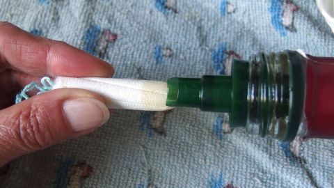 Eine Hand hält ein Anwendungshilfsmittel, das in eine Flasche eingetaucht wird, um Soforthilfe bei Scheidenpilz zu geben.