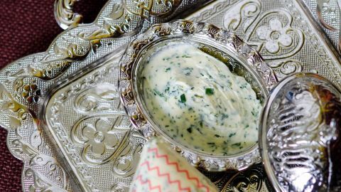 Ein silbernes Tablett hält frische Kräuterbutter, die in einer eleganten Schale angerichtet ist, umgeben von einem feinen Stoff.