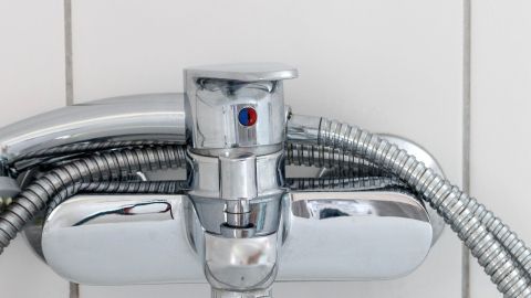 Ein glänzender Wasserhahn steht im Vordergrund und wird von flexiblen Schläuchen gehalten, umgeben von weißen Keramikfliesen.