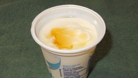 Ein Becher Naturjoghurt mit flüssigem Honig steht auf einem grünen Untergrund und wirkt frisch und appetitlich.