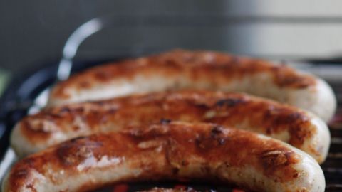 Auf dem Grill liegen mehrere knusprige Bratwürste, die appetitlich gebräunt sind und mit rauchigen Aromen umgeben sind.