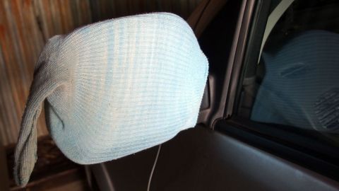 Ein frostsicherer Autospiegel ist mit einem blauen Tuch abgedeckt, während er an einem geparkten Auto befestigt ist.