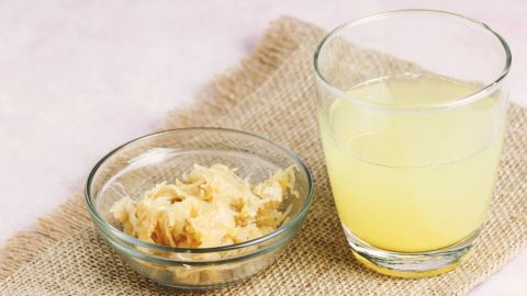 Wenn du an Verstopfung leidest, hilft Sauerkrautsaft! Nimm diesen einmal täglich vor deiner Hauptmahlzeit zu dir und die Verstopfung wird sich lösen. Ein Glas mit hellem Saft steht neben einer Schüssel mit zerkleinertem Ingwer auf einem Jutesack. Hausmittel gegen Verstopfung.