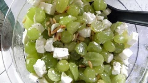 Ein grüner Weintraubensalat mit Schafskäse und gerösteten Pinienkernen in einer klaren Schüssel.