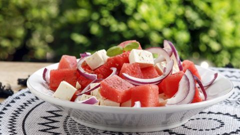 Ein frischer Melonensalat mit Schafskäse und roten Zwiebeln bleibt auf einem dekorativen Tischmuster.