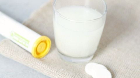 Ein Glas mit milchähnlichem Getränk steht auf einem Stoffuntergrund, neben einer Calcium- und Magnesiumtablette.