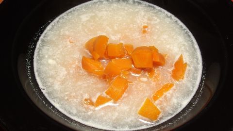 Eine cremige Karottensuppe mit kleinen Karottenstücken schwimmt in einer weißen Flüssigkeit auf einem schwarzen Teller.