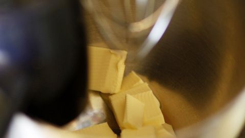 Kalte Butterstückchen liegen in einer Rührschüssel, während ein Mixer bereit ist, sie zu verarbeiten, um Kuchenteig zu machen.