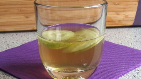 Ein Glas Wodka-Gurke mit Gurkenscheiben liegt auf einem lila Untersetzer in einer modernen Küche.