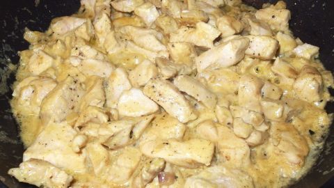 Hühnchenstücke schmoren in einer cremigen Currysoße in einer Pfanne, umgeben von einem dunklen Hintergrund.