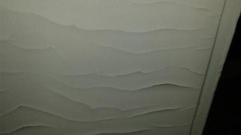 Eine Backofentür zeigt abgeblätterte, gewellte Lackschichten im schwachen Licht einer Küche, die Reinigung benötigt.