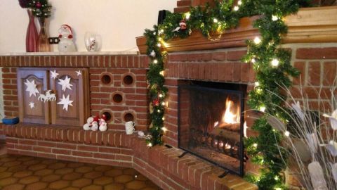 Ein Kamin mit flammendem Feuer in einem gemütlichen Raum, umgeben von Weihrauch und dekorativer Weihnachtsbeleuchtung.