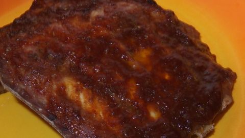 Im Hintergrund liegt ein glänzendes Stück Barbecue-Spareribs auf einem leuchtend orangefarbenen Teller, appetitlich zubereitet.