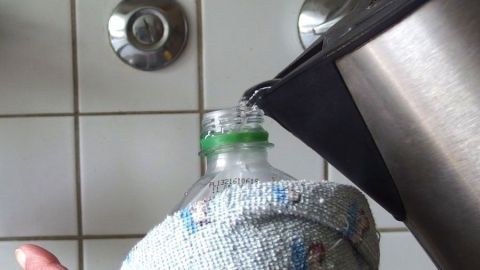 Eine handgehaltene PET-Trinkflasche wird mit heißem Wasser gefüllt, während sie mit einem Handtuch umwickelt ist.