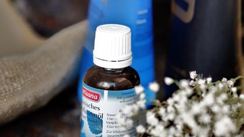 Eine Flasche mit Minzöl steht neben blauer Badecreme auf einer rustikalen Oberfläche, umgeben von einem Handtuch und kleinen Blumen.