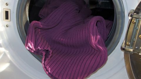 Ein lila Pullover liegt in einer Waschmaschine, die gerade läuft, symbolisiert modernes Wäschewaschen heute.