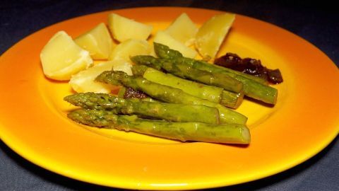Grüner Spargel liegt auf einem bunten Teller neben Kartoffeln und einer dunklen Sauce, alles appetitlich angerichtet.