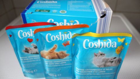 Katzenfutterpäckchen stehen auf einer weißen Fläche neben einer Verpackung, die Kühlung für frische Tiernahrung empfiehlt.