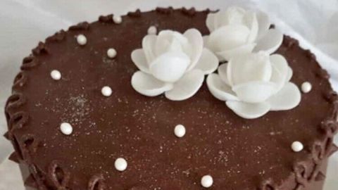 Eine Schokoladentorte mit zarter Füllung steht elegant auf einer weißen Unterlage, dekoriert mit weißen Blüten und Perlen.
