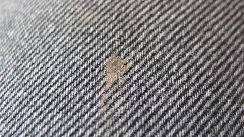Ein Fleck auf grauem Stoff zeigt, wie Gallseife als effektiver Fleckenkiller eingesetzt werden kann.