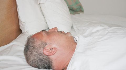 Ein Mann liegt auf einem Bett, schläft ohne Kissen und scheint entspannt zu sein, um Migräne zu bekämpfen.