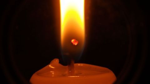 Eine brennende Kerze erzeugt Licht und Wärme, während ihr Wachs schmilzt und sich langsam am Rand ansammelt.