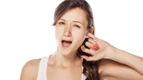 Eine Frau hält sich schmerzhaft das Ohr und zeigt Anzeichen von Unbehagen, während sie sich in einem hellen Raum befindet.