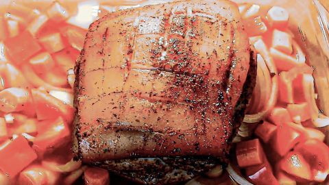 Ein saftiger Schweineschmorbraten liegt in einer Auflaufform, umgeben von buntem Gemüse in einer aromatischen Brühe.