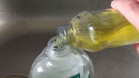 Eine Hand dosiert sparsames Spülmittel aus einer Flasche in einen Behälter über einem Spülbecken.