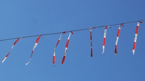 Bunte Wimpel wehen im Wind und sollen dazu dienen, Tauben vom Balkon fernzuhalten, unter einem klaren blauen Himmel.
