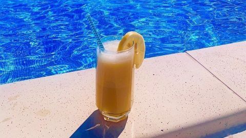 Ein kalter Engel Cocktail steht am Rand eines blauen Schwimmbeckens, mit einem klaren Blick auf das Wasser und die umliegende Landschaft.