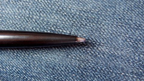 Ein Kugelschreiber liegt auf einem blauen Jeansstoff, wobei die Spitze des Stifts auf einem kleinen Riss zeigt.