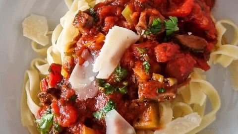Ein Teller mit frischen Nudeln ist mit einer bunten Tomatensauce und Parmesan belegt, umgeben von einem einladenden Ambiente.