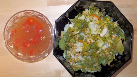 Frischer Salat in einer schwarzen Schüssel neben einer transparenten Schüssel mit Salatsoßengewürz.