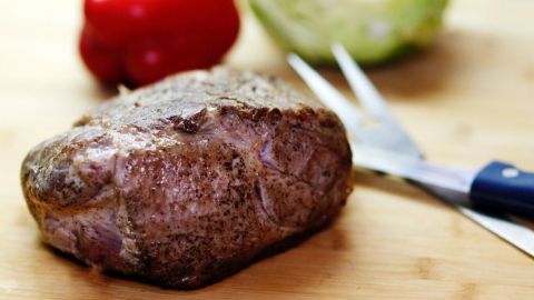 Ein saftiger Nackenbraten liegt auf einem Holzbrett, umgeben von frischen Paprika und Kohl, bereit zum Servieren.