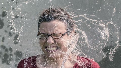 Eine Person mit Brille wird von Wasserspritzern getroffen, während sie im Freien steht und kühlende Erfrischung erlebt.