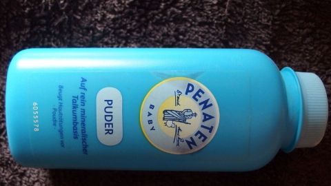 Eine Flasche Babypuder steht auf einem braunen Teppich, bereit, gegen fettige Haare eingesetzt zu werden.