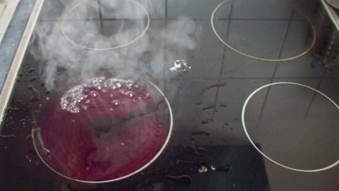 Ein Glaskeramik-Kochfeld zeigt Dampf und eine rote Flüssigkeit, die über die heiße Fläche kocht und spritzt.