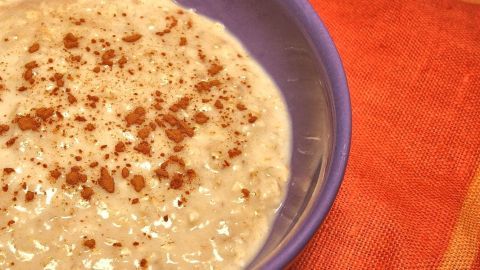 Ein cremiges Schlemmer-Porridge liegt in einer lila Schüssel, garniert mit einer Knuspermischung, auf einem bunten Tischcloth.