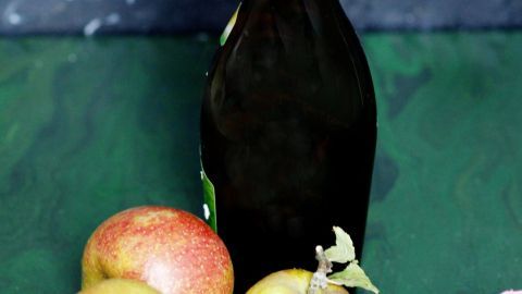 Eine Flasche Apfelessig steht neben frischen Äpfeln auf einem grünen Hintergrund, ideal für die Pflege reiner Haut.