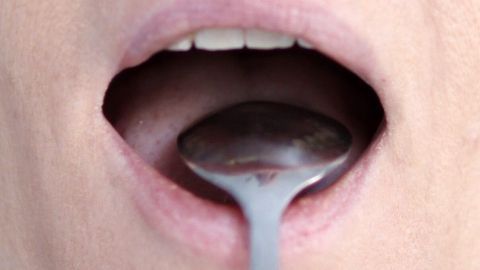 Ein Löffel wird in einen offenen Mund gehalten, um gegen Mundgeruch zu wirken. Das Umfeld ist neutral ohne Ablenkungen.